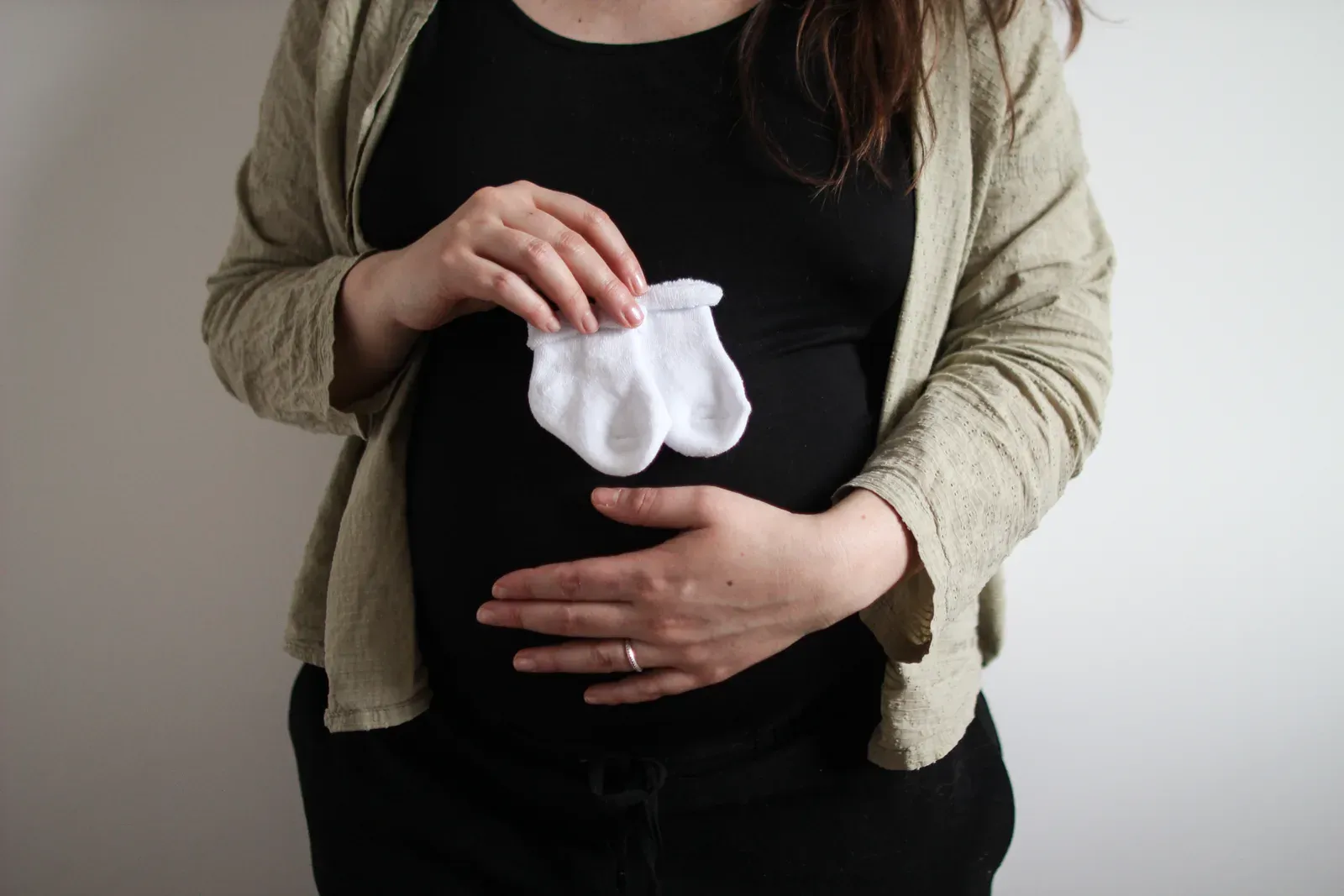 Femme enceinte tenant délicatement de petites chaussettes de bébé contre son ventre